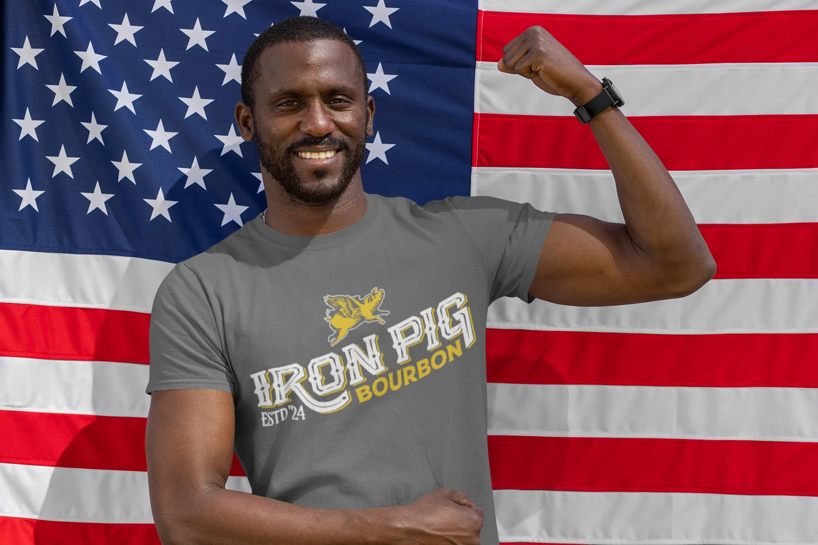 Smiling man flexing in a gray Iron Pig Bourbon T-shirt in front of an American flag